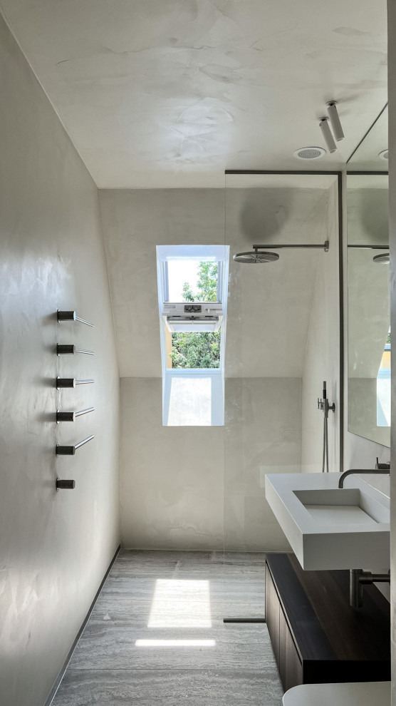 Inredning av ett modernt mellanstort vit vitt badrum med dusch, med en kantlös dusch, en vägghängd toalettstol, grå väggar, travertin golv, ett väggmonterat handfat, bänkskiva i akrylsten, grått golv och med dusch som är öppen