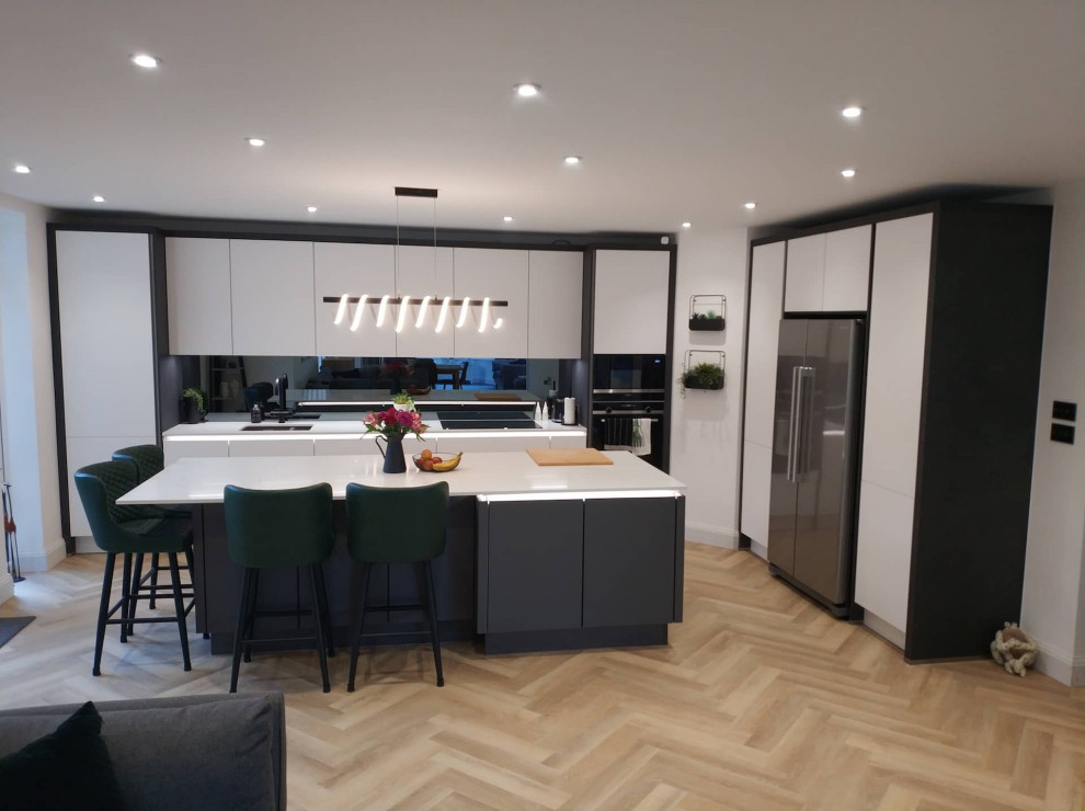 Large contemporary l-shaped open plan kitchen in Hertfordshire with flat-panel cabinets, white cabinets, quartz worktops, light hardwood flooring, an island, beige floors and white worktops.