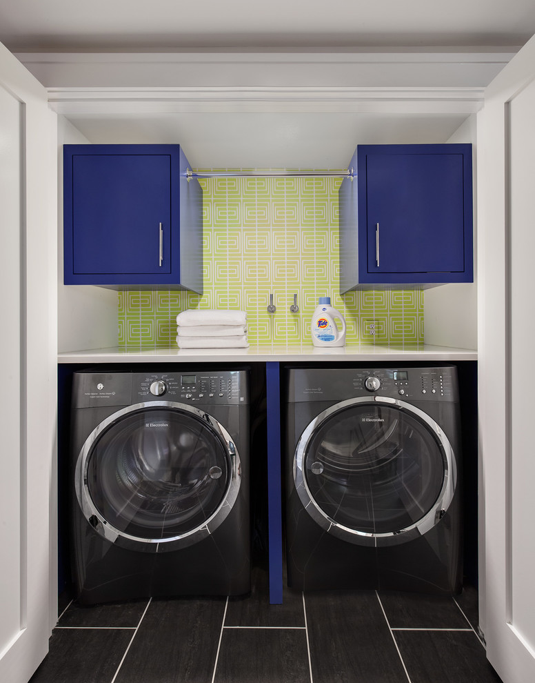 Small transitional laundry room in New York with flat-panel cabinets, blue cabinets, green walls, a side-by-side washer and dryer and black floor.
