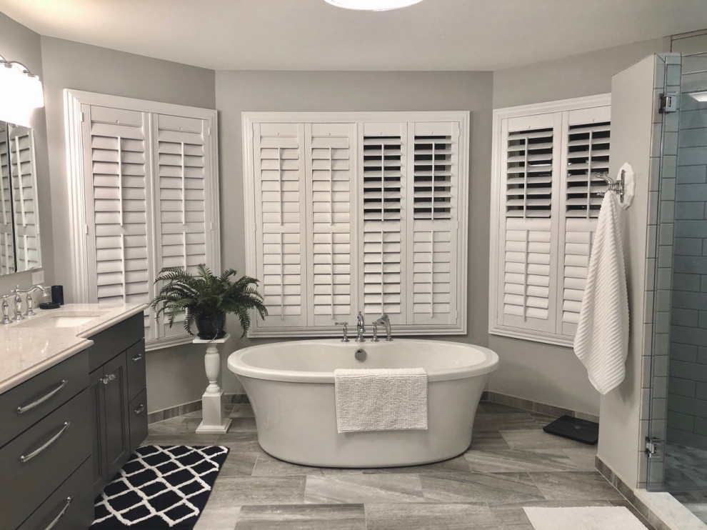 Photo of a large traditional master bathroom in St Louis with recessed-panel cabinets, grey cabinets, a freestanding tub, an alcove shower, a two-piece toilet, white tile, subway tile, grey walls, an undermount sink, grey floor, a hinged shower door, grey benchtops, a niche, a shower seat, an enclosed toilet and a built-in vanity.