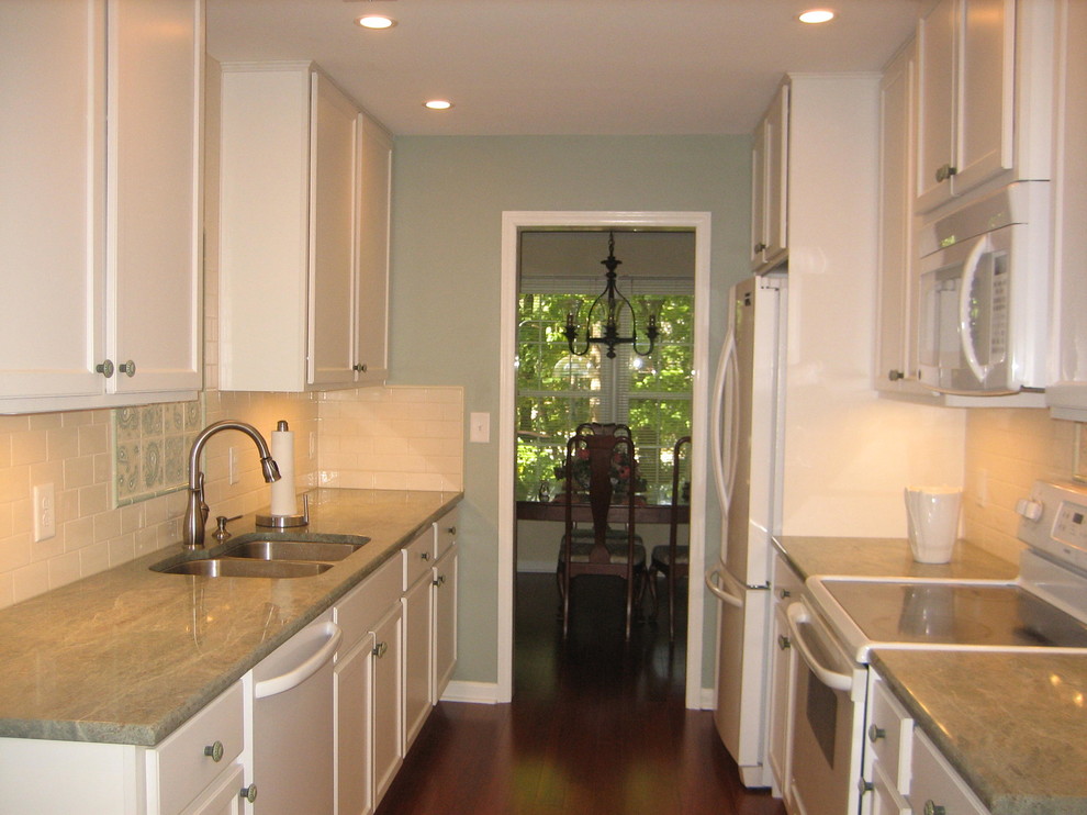 Small transitional galley dark wood floor and brown floor enclosed kitchen photo in Raleigh with a double-bowl sink, recessed-panel cabinets, white cabinets, marble countertops, white backsplash, subway tile backsplash, white appliances, no island and beige countertops