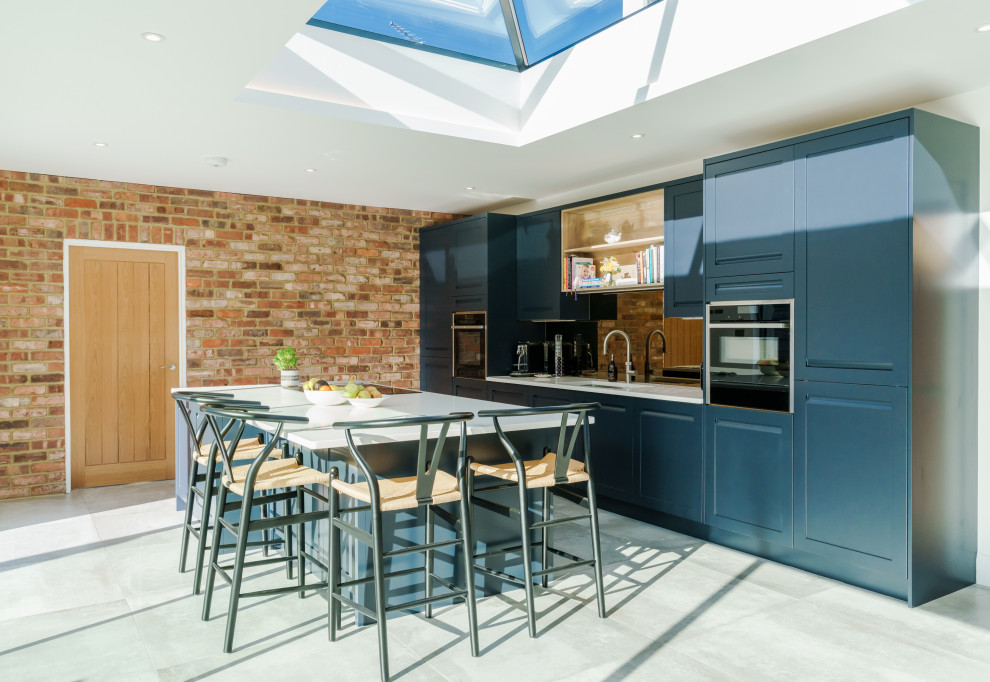 Traditional galley kitchen in Buckinghamshire with a submerged sink, shaker cabinets, blue cabinets, mirror splashback, black appliances, a breakfast bar, grey floors and white worktops.