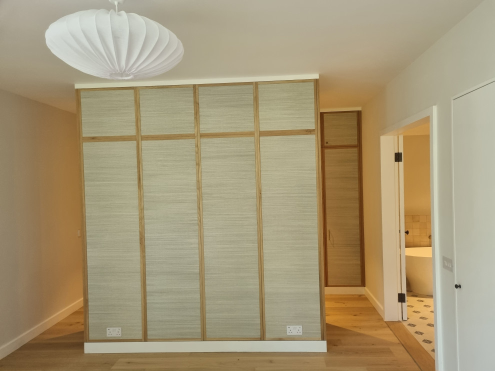 Example of a large minimalist master plywood floor bedroom design in London with beige walls