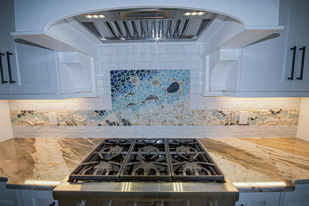 Eat-in kitchen - large coastal single-wall eat-in kitchen idea with a farmhouse sink, shaker cabinets, white cabinets, granite countertops, multicolored backsplash, an island and multicolored countertops