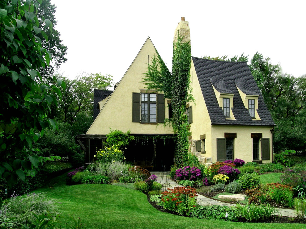 Large traditional two-storey concrete yellow house exterior in Chicago with a clipped gable roof and a shingle roof.