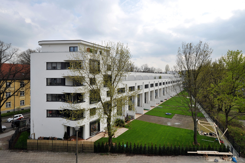This is an example of a large contemporary three-storey stucco white townhouse exterior in Berlin with a flat roof and a green roof.