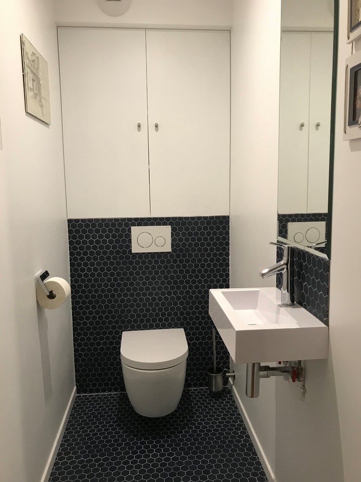 Design ideas for a mid-sized contemporary powder room in Bordeaux with beaded inset cabinets, white cabinets, a wall-mount toilet, blue tile, terra-cotta tile, white walls, terra-cotta floors, a wall-mount sink, engineered quartz benchtops and blue floor.