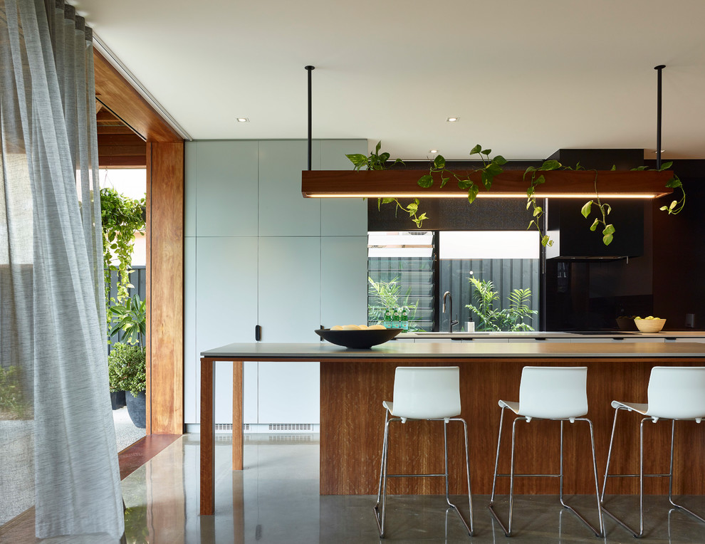 Photo of a contemporary galley kitchen in Brisbane with an undermount sink, flat-panel cabinets, medium wood cabinets, black splashback, concrete floors, with island, grey floor and grey benchtop.