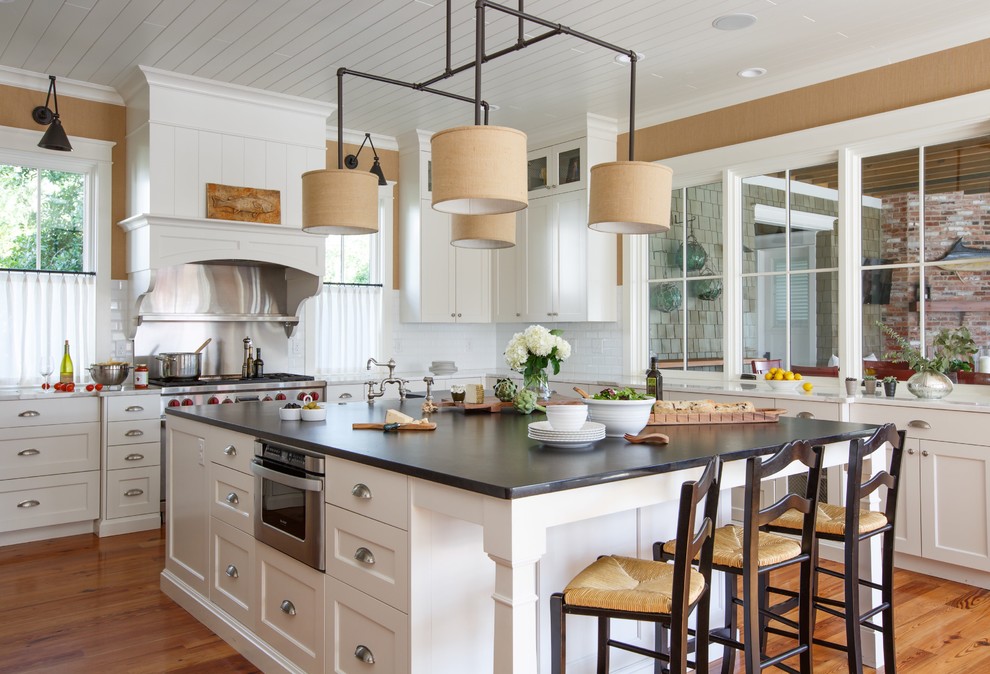Beach style l-shaped eat-in kitchen in Jacksonville with shaker cabinets, white cabinets, white splashback, stainless steel appliances, medium hardwood floors, with island, brown floor and black benchtop.