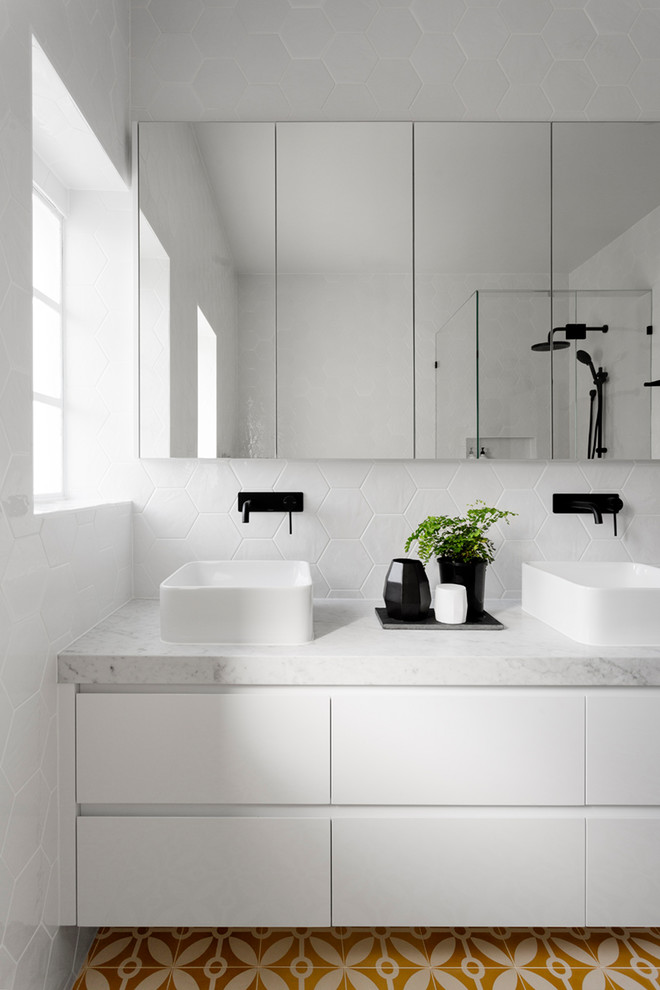 Inspiration for a large contemporary master bathroom in Melbourne with flat-panel cabinets, white cabinets, a drop-in tub, a corner shower, a one-piece toilet, white tile, ceramic tile, white walls, cement tiles, a vessel sink, marble benchtops, yellow floor and a hinged shower door.