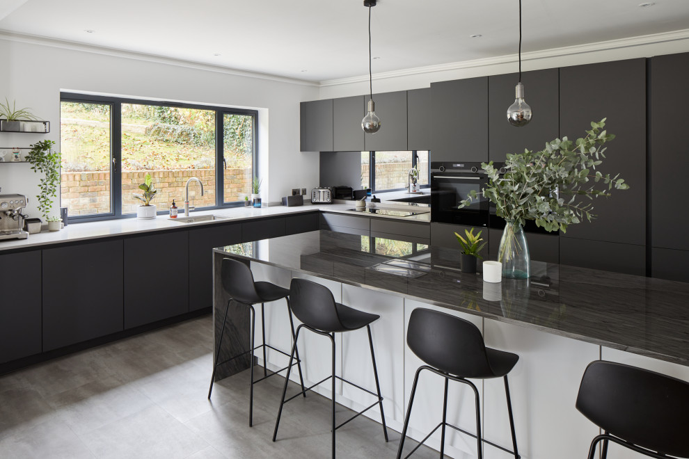 Photo of a medium sized contemporary l-shaped kitchen/diner in London with a submerged sink, flat-panel cabinets, grey cabinets, glass sheet splashback, stainless steel appliances and an island.