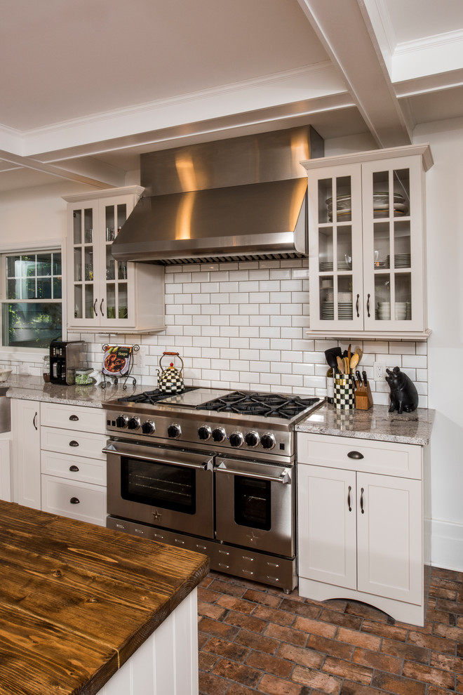 This is an example of a large country l-shaped eat-in kitchen in New York with a farmhouse sink, shaker cabinets, white cabinets, granite benchtops, white splashback, subway tile splashback, stainless steel appliances, terra-cotta floors and with island.