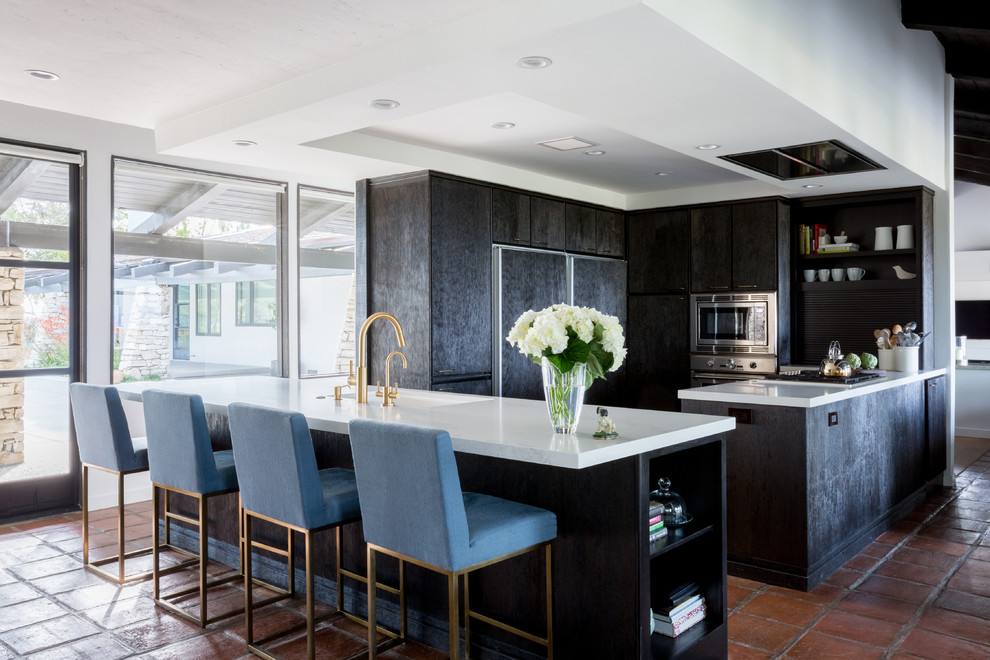 Design ideas for a midcentury u-shaped eat-in kitchen in Los Angeles with an undermount sink, flat-panel cabinets, black cabinets, stainless steel appliances, terra-cotta floors, with island, brown floor and white benchtop.