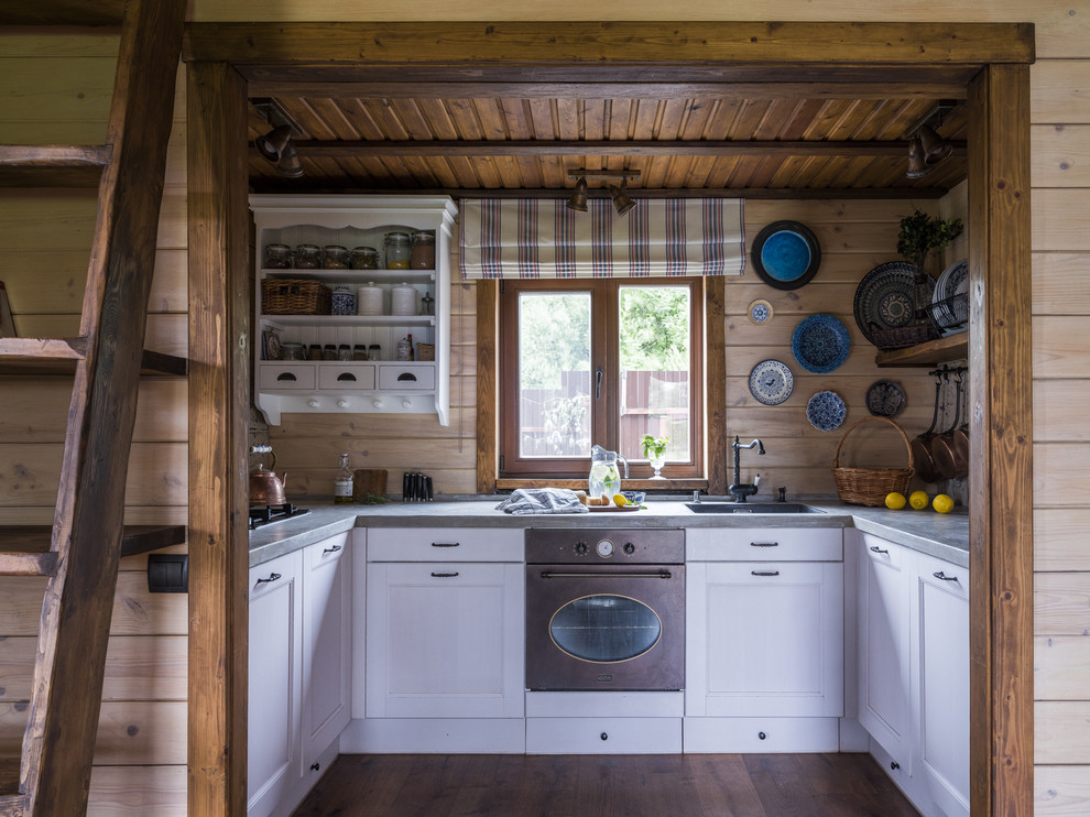 Photo of a mid-sized country u-shaped open plan kitchen in Moscow with an undermount sink, beaded inset cabinets, white cabinets, concrete benchtops, beige splashback, timber splashback, coloured appliances, dark hardwood floors, no island, brown floor and grey benchtop.