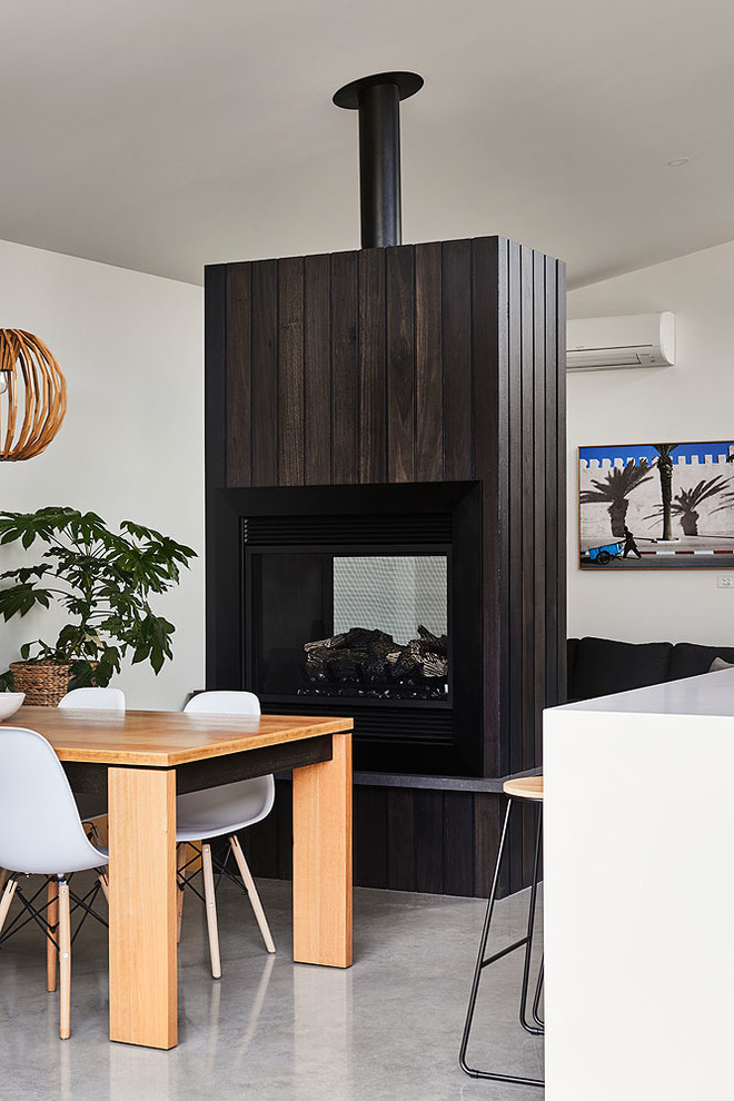 Photo of a beach style open plan dining in Geelong with white walls, concrete floors, a two-sided fireplace, a wood fireplace surround and grey floor.