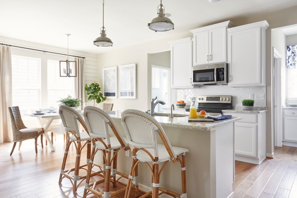 Design ideas for a beach style eat-in kitchen in Other with an undermount sink, recessed-panel cabinets, white cabinets, white splashback, stainless steel appliances, light hardwood floors, with island and grey benchtop.