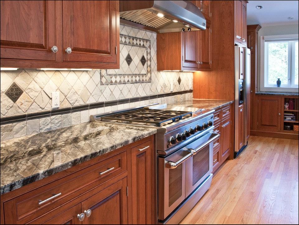 Large traditional l-shaped eat-in kitchen in Boston with raised-panel cabinets, medium wood cabinets, granite benchtops, an undermount sink, white splashback, ceramic splashback, stainless steel appliances, light hardwood floors and with island.