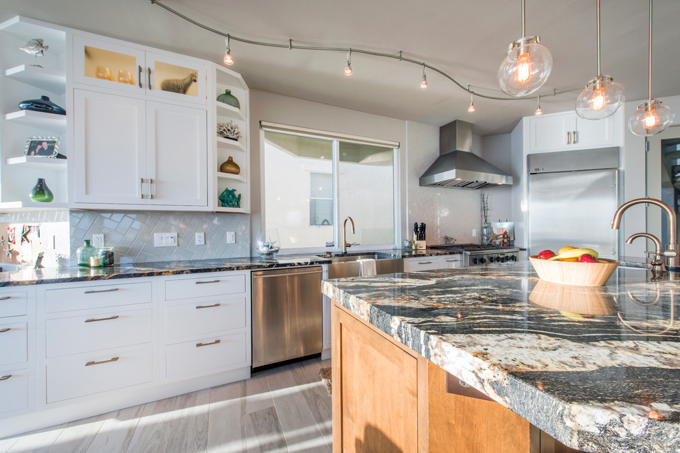 Photo of a mid-sized modern open plan kitchen in San Diego with a farmhouse sink, flat-panel cabinets, white cabinets, granite benchtops, grey splashback, subway tile splashback, stainless steel appliances, porcelain floors and with island.