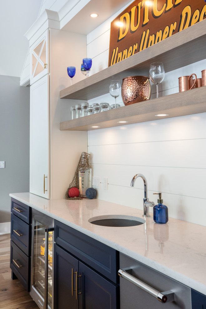 This is an example of a mid-sized beach style galley wet bar in Milwaukee with an undermount sink, flat-panel cabinets, white cabinets, quartz benchtops, white splashback, shiplap splashback, medium hardwood floors, brown floor and white benchtop.