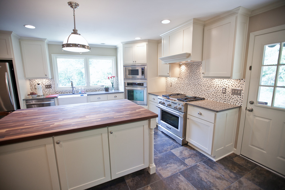 This is an example of a large country l-shaped eat-in kitchen in Nashville with a farmhouse sink, recessed-panel cabinets, white cabinets, wood benchtops, multi-coloured splashback, mosaic tile splashback, stainless steel appliances, porcelain floors and with island.