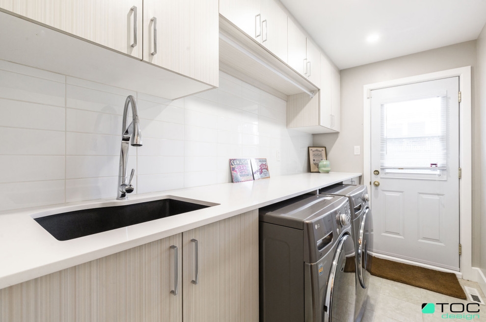 Photo of a large contemporary galley utility room in Montreal with an undermount sink, flat-panel cabinets, light wood cabinets, quartz benchtops, white splashback, cement tile splashback, grey walls, ceramic floors, a side-by-side washer and dryer, beige floor and white benchtop.