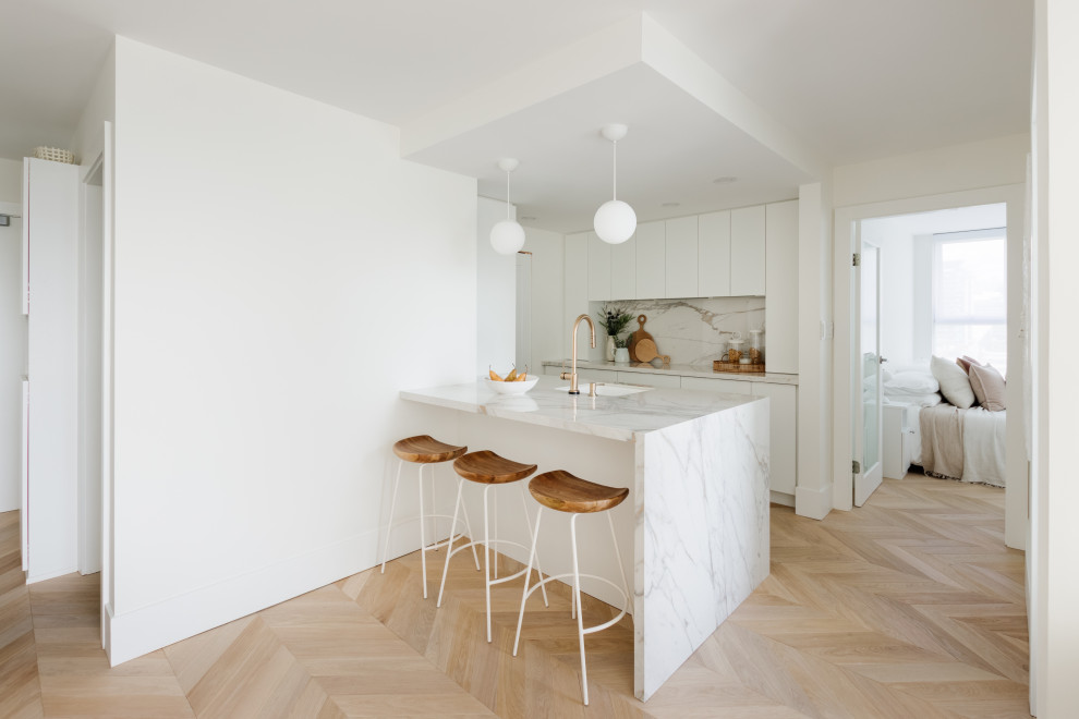 Idéer för att renovera ett litet skandinaviskt vit vitt kök, med en undermonterad diskho, släta luckor, vita skåp, marmorbänkskiva, vitt stänkskydd, stänkskydd i porslinskakel, integrerade vitvaror, ljust trägolv, en halv köksö och beiget golv
