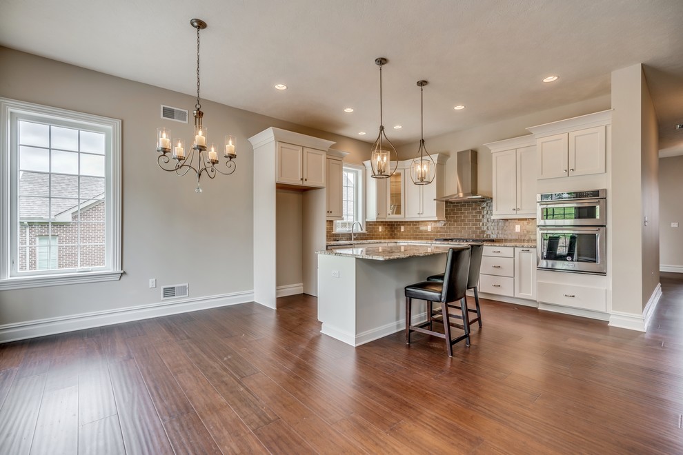 Transitional l-shaped bamboo floor eat-in kitchen photo with an undermount sink, flat-panel cabinets, white cabinets, granite countertops, brown backsplash, subway tile backsplash, stainless steel appliances, an island and brown countertops