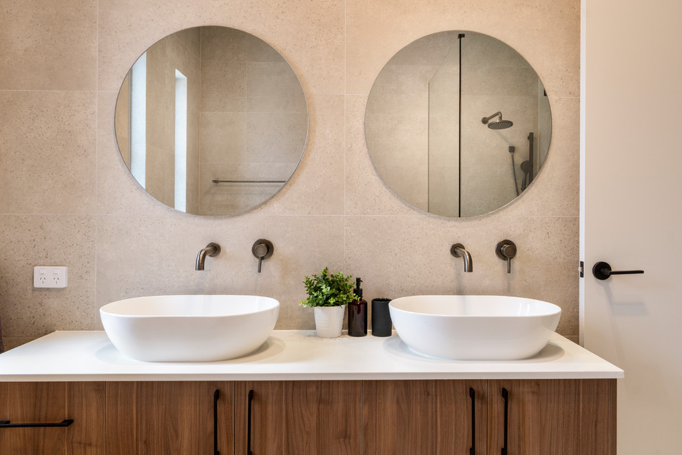 Photo of a large contemporary master bathroom in Sydney with flat-panel cabinets, medium wood cabinets, a freestanding tub, an open shower, a two-piece toilet, beige tile, ceramic tile, beige walls, ceramic floors, a vessel sink, engineered quartz benchtops, beige floor, a hinged shower door and white benchtops.