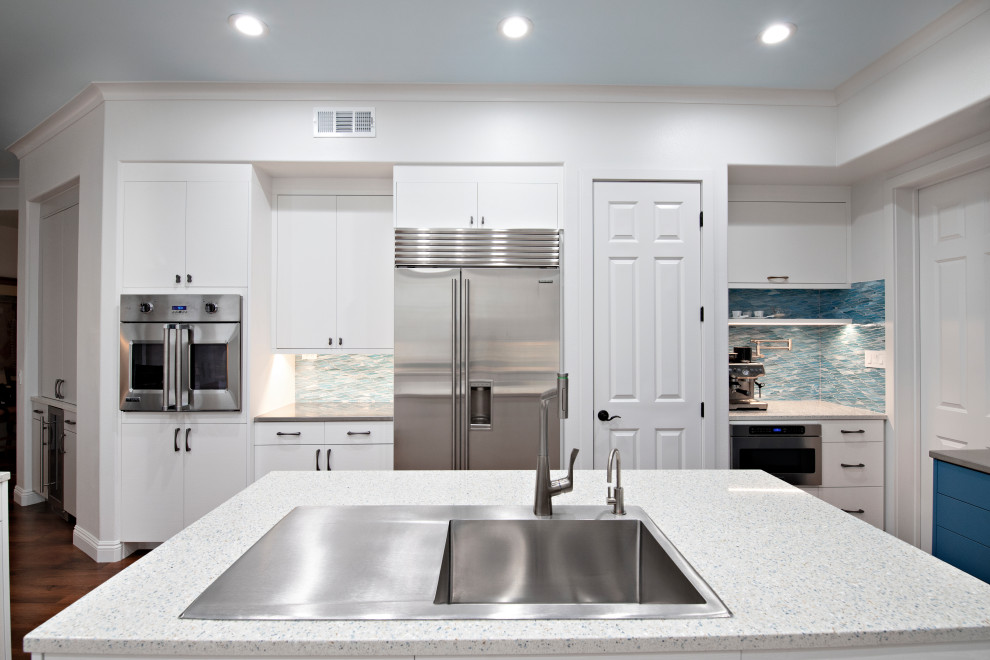 Large trendy u-shaped medium tone wood floor eat-in kitchen photo in San Diego with a drop-in sink, flat-panel cabinets, white cabinets, stainless steel countertops, blue backsplash, mosaic tile backsplash, stainless steel appliances, an island and white countertops