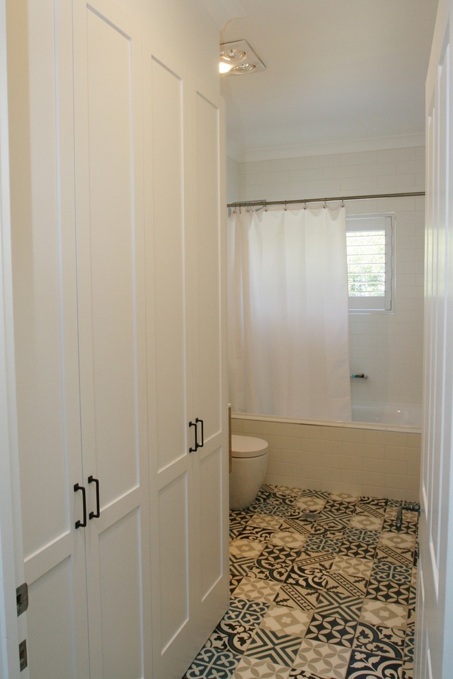 Photo of a mid-sized traditional single-wall utility room in Sydney with shaker cabinets, white cabinets, white splashback, ceramic splashback, solid surface benchtops, white walls, ceramic floors, an undermount sink, white benchtop, an integrated washer and dryer and multi-coloured floor.