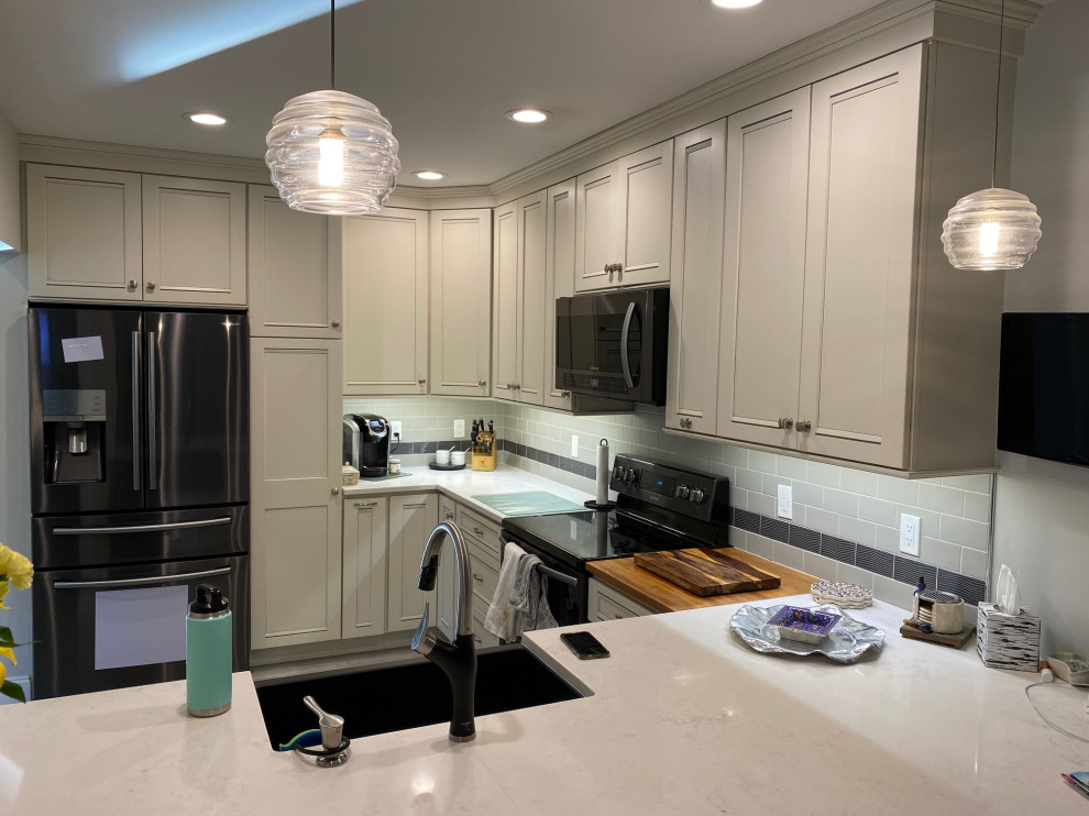 Inspiration for a mid-sized transitional u-shaped porcelain tile and gray floor eat-in kitchen remodel in Burlington with a farmhouse sink, recessed-panel cabinets, white cabinets, quartz countertops, gray backsplash, subway tile backsplash, stainless steel appliances and white countertops