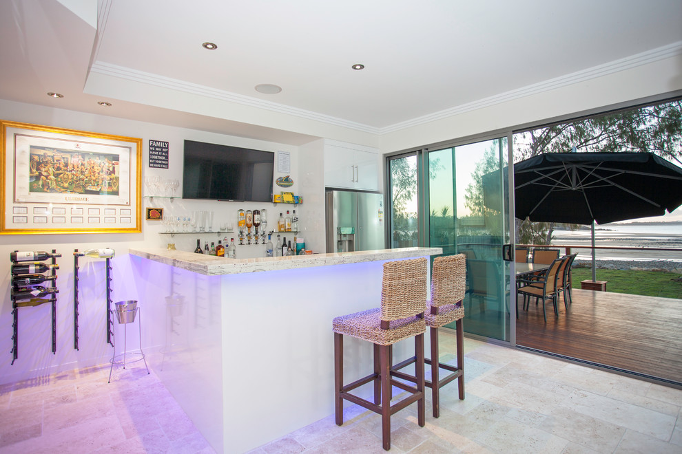 Photo of a mid-sized beach style l-shaped seated home bar in Other with flat-panel cabinets, white cabinets, granite benchtops, travertine floors, beige floor and white benchtop.