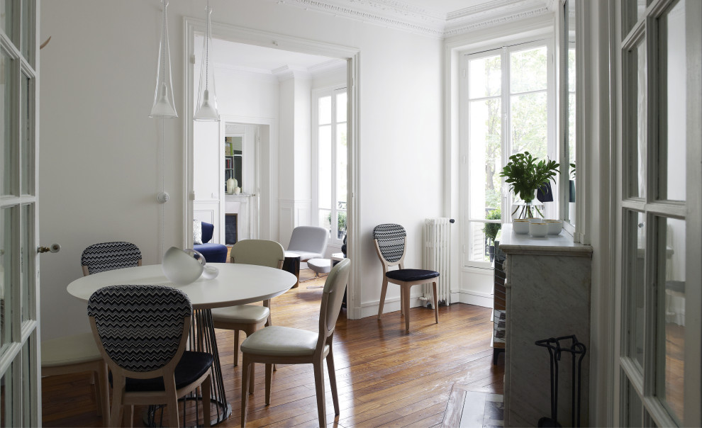 Cette photo montre une salle à manger ouverte sur le salon tendance de taille moyenne avec un mur blanc, un sol en bois brun, une cheminée standard, un manteau de cheminée en pierre et un sol marron.