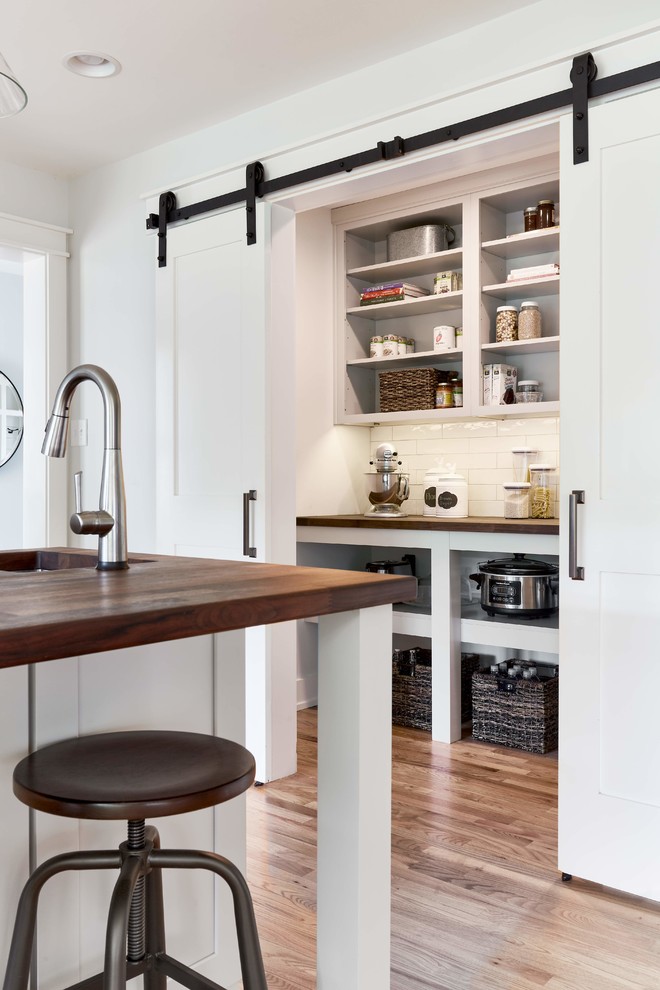 Large country kitchen pantry in Richmond with white cabinets, wood benchtops, white splashback, subway tile splashback, medium hardwood floors, brown floor, brown benchtop, a farmhouse sink, stainless steel appliances, with island and shaker cabinets.