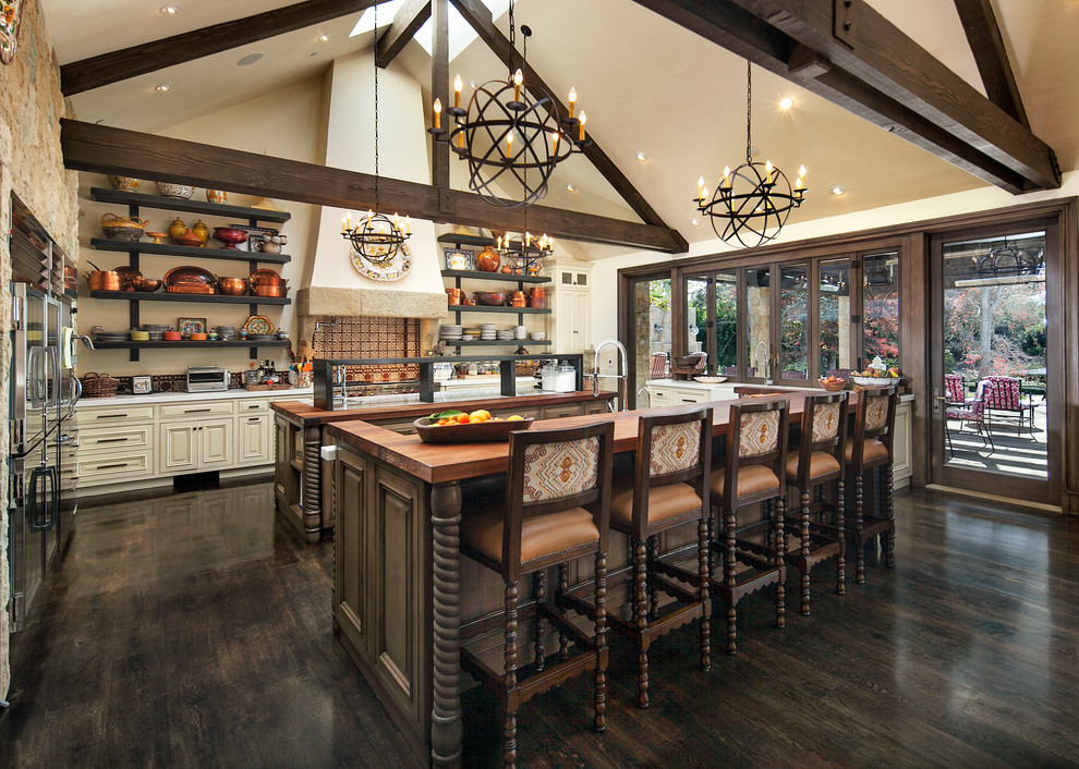 Example of a tuscan dark wood floor and brown floor kitchen design in Santa Barbara with stainless steel appliances, two islands, raised-panel cabinets, beige cabinets, multicolored backsplash and white countertops