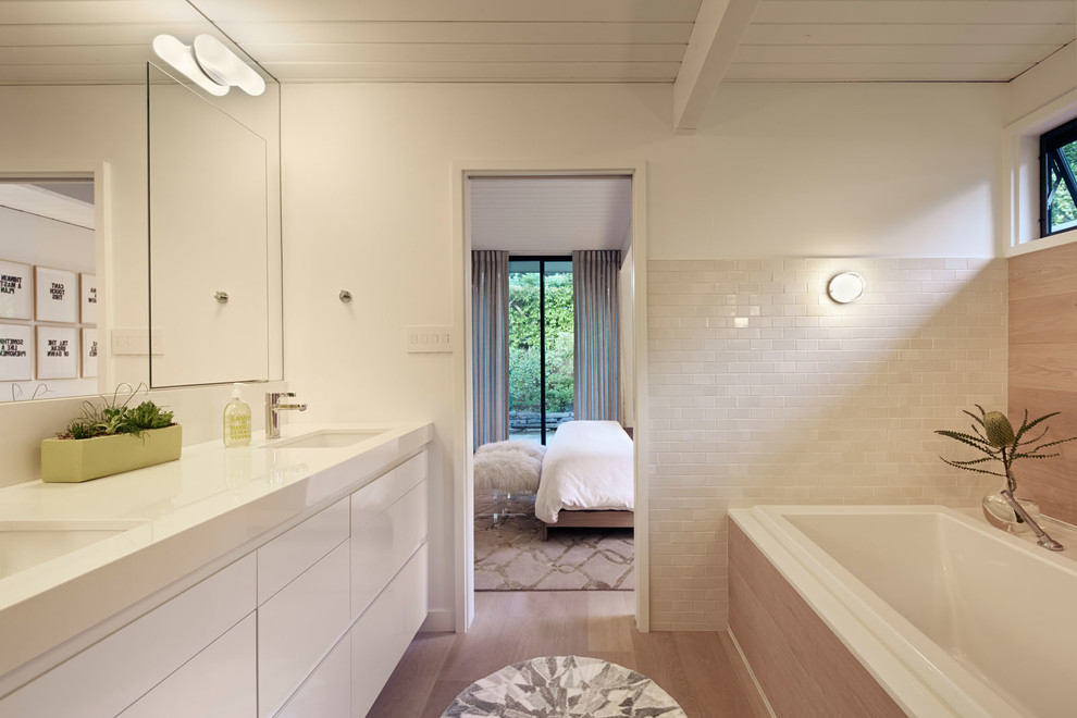 Inspiration for a midcentury bathroom in San Francisco with an undermount sink, flat-panel cabinets, white cabinets, a drop-in tub and beige tile.