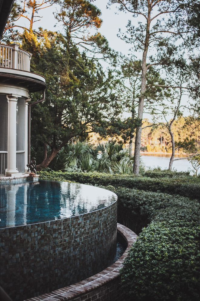 Mid-sized backyard custom-shaped infinity pool in Charleston with brick pavers.