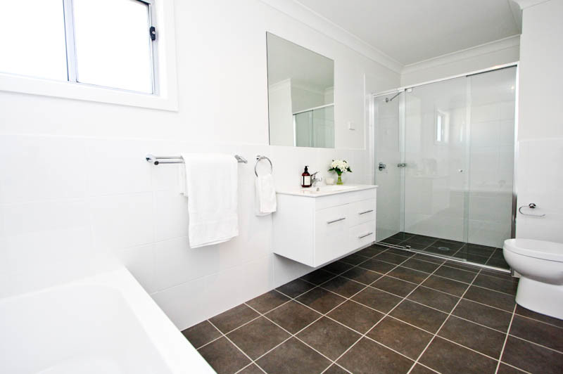Photo of a mid-sized contemporary master bathroom in Newcastle - Maitland with white cabinets, a drop-in tub, a corner shower, a wall-mount toilet, white tile, ceramic tile, white walls, ceramic floors, a wall-mount sink and solid surface benchtops.
