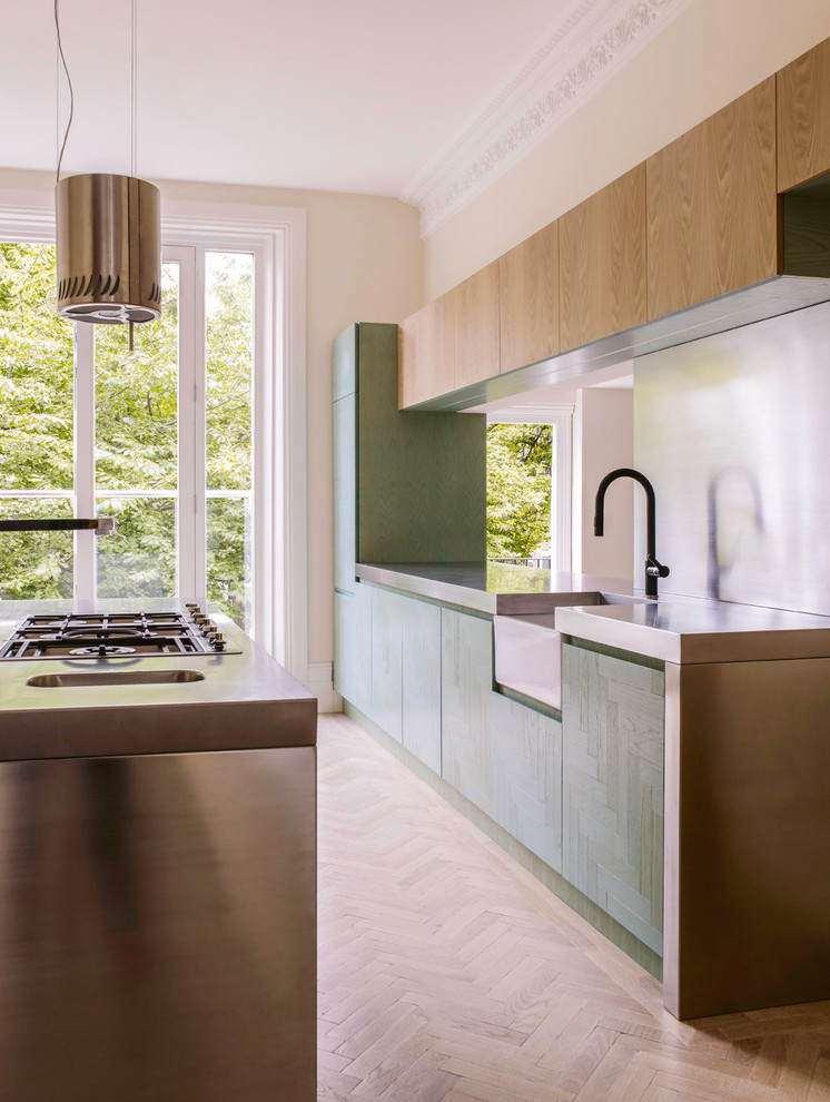 Inspiration for a contemporary kitchen/diner with a belfast sink, turquoise cabinets, stainless steel worktops, metallic splashback, stainless steel appliances, beige walls, light hardwood flooring and an island.