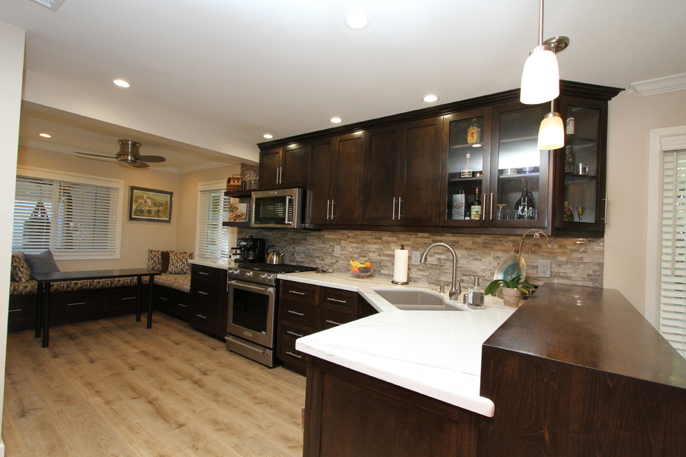 Example of a small transitional l-shaped light wood floor and beige floor open concept kitchen design in Orange County with an undermount sink, shaker cabinets, dark wood cabinets, quartz countertops, beige backsplash, glass sheet backsplash, stainless steel appliances and no island