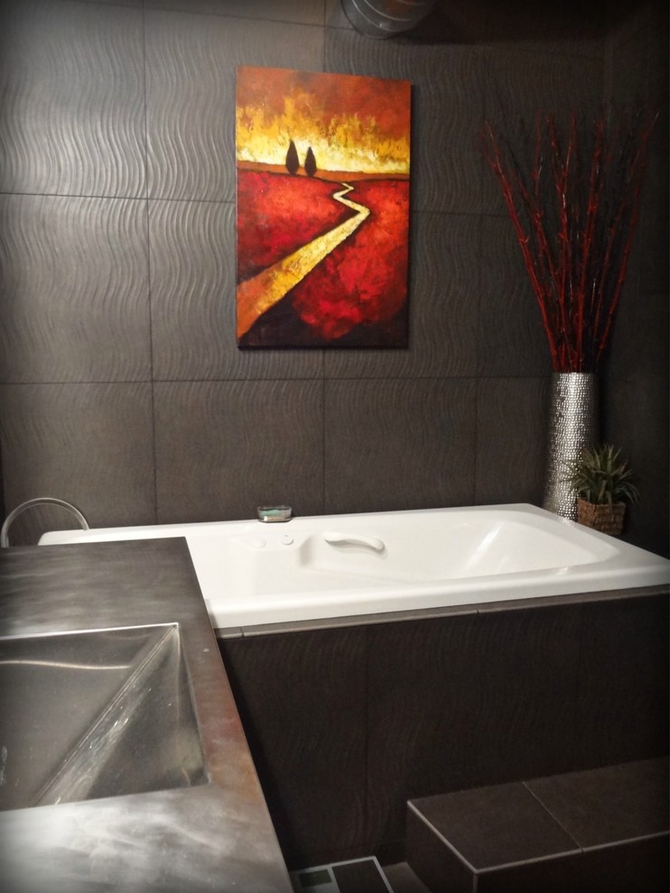 Inspiration for a mid-sized industrial master bathroom in Portland with an integrated sink, flat-panel cabinets, stainless steel benchtops, a drop-in tub, an open shower, a one-piece toilet, gray tile, porcelain tile, grey walls, concrete floors and black cabinets.