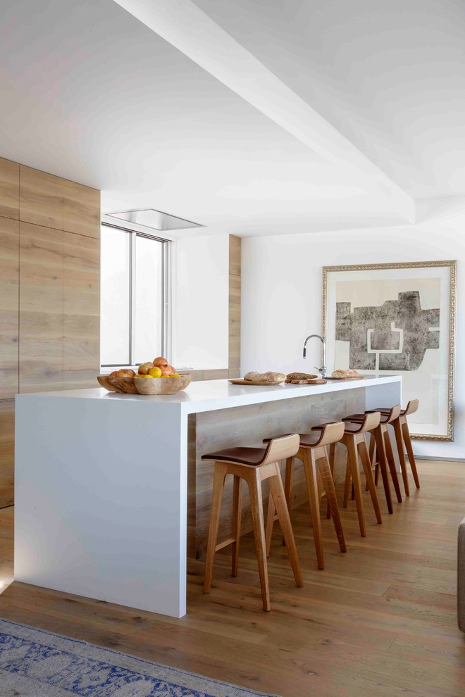 Contemporary galley open plan kitchen in Madrid with flat-panel cabinets, medium wood cabinets, window splashback, panelled appliances, with island, beige floor and white benchtop.