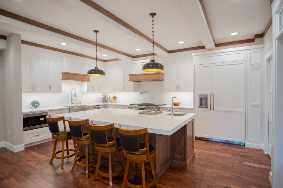 Large transitional u-shaped medium tone wood floor, brown floor and exposed beam eat-in kitchen photo in Seattle with an island, a farmhouse sink, shaker cabinets, white cabinets, quartz countertops, white backsplash, ceramic backsplash, stainless steel appliances and white countertops
