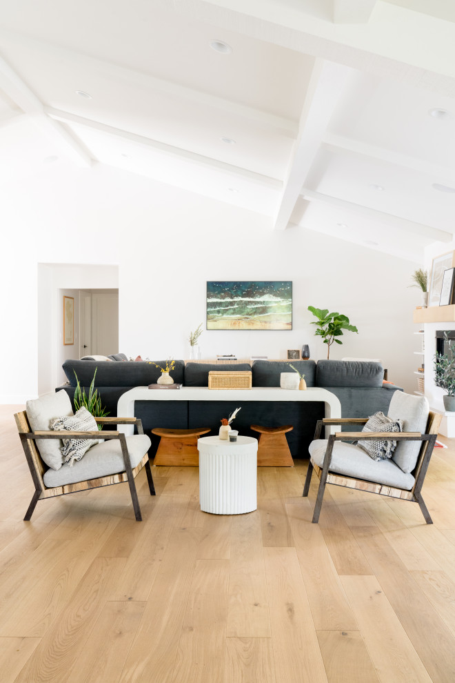 This is an example of a medium sized scandinavian open plan games room in Orange County with white walls, light hardwood flooring, a standard fireplace, a plastered fireplace surround, a wall mounted tv, brown floors and a vaulted ceiling.