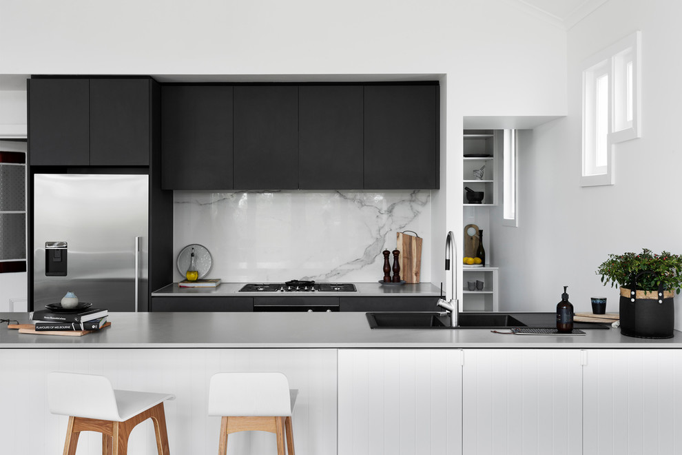 Inspiration for a mid-sized contemporary galley open plan kitchen in Melbourne with an integrated sink, flat-panel cabinets, black cabinets, concrete benchtops, white splashback, marble splashback, stainless steel appliances, medium hardwood floors, a peninsula, brown floor and white benchtop.
