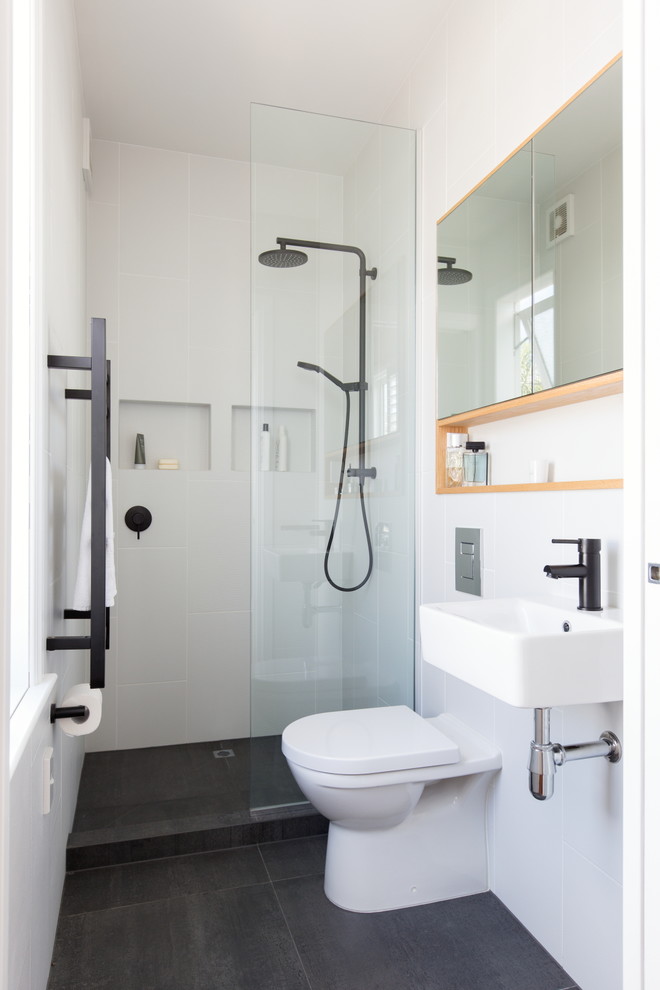 Photo of a small eclectic bathroom in Auckland with an open shower, a wall-mount toilet, black and white tile, porcelain tile, light wood cabinets, white walls, porcelain floors and a wall-mount sink.