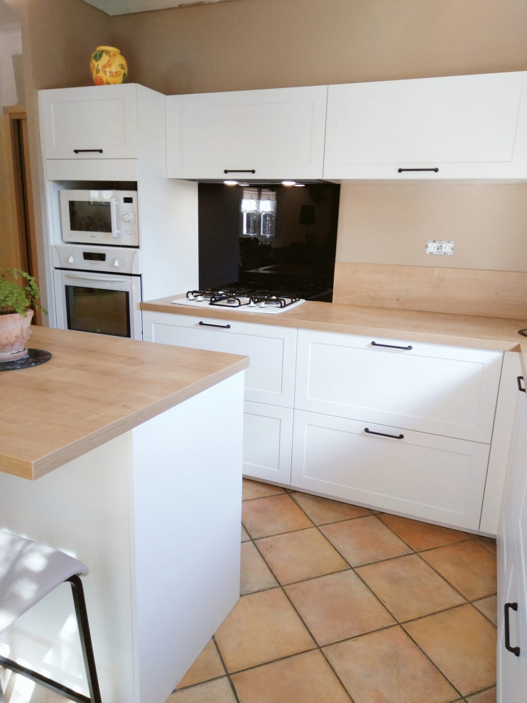 This is an example of a large classic l-shaped open plan kitchen in Marseille with a single-bowl sink, shaker cabinets, white cabinets, laminate countertops, brown splashback, white appliances, terracotta flooring, an island, brown floors and brown worktops.