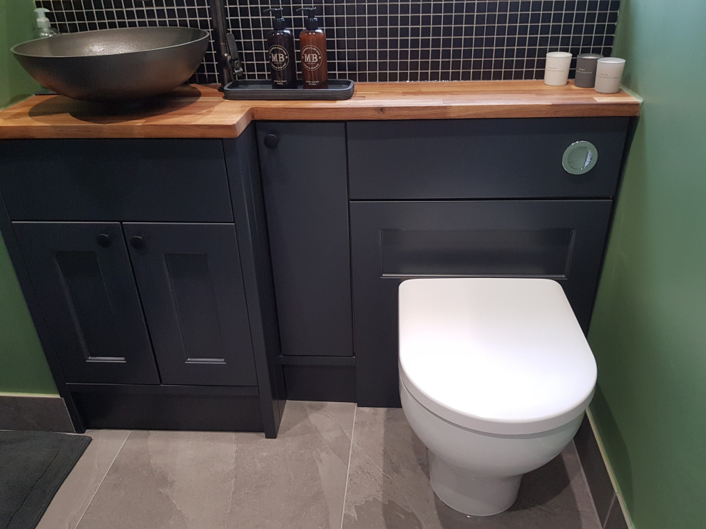 Bathroom - small contemporary kids' black tile and mosaic tile single-sink bathroom idea in Oxfordshire with shaker cabinets, blue cabinets, a one-piece toilet, green walls, a vessel sink, wood countertops, multicolored countertops and a built-in vanity