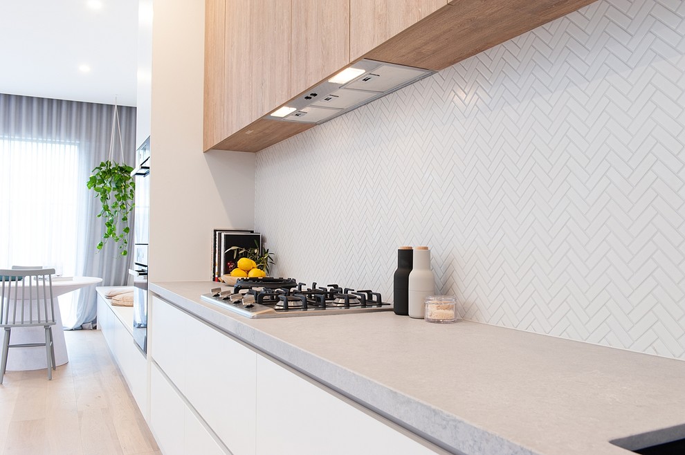 This is an example of an expansive scandinavian galley open plan kitchen in Melbourne with an integrated sink, open cabinets, light wood cabinets, quartz benchtops, grey splashback, marble splashback, black appliances, light hardwood floors, with island and grey benchtop.