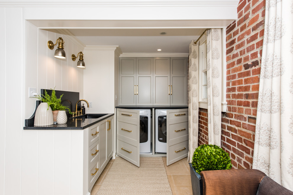 Inspiration for a small transitional l-shaped laundry room in DC Metro with an undermount sink, recessed-panel cabinets, grey cabinets, granite benchtops, white walls, ceramic floors, a concealed washer and dryer and beige floor.